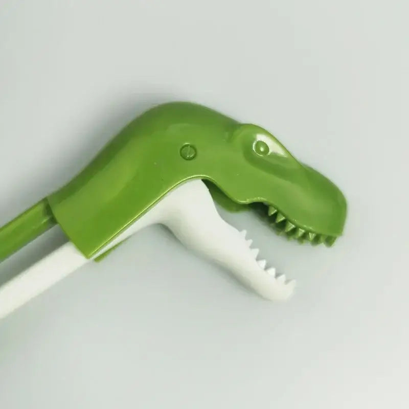 Green plastic dinosaur-shaped toothbrush with white bristles featuring sharp teeth for kids training dino chopsticks decorbites