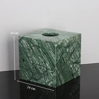 Green marble tissue box with natural stone pattern and circular opening in a marble bathroom set with gold accents