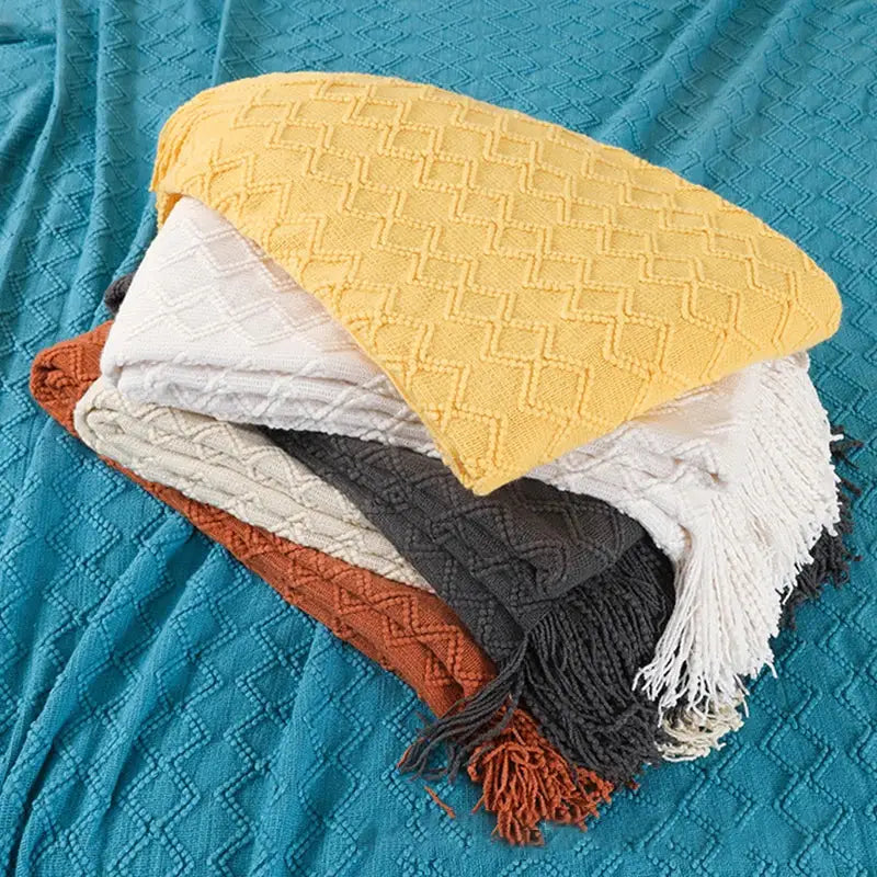 Stack of cozy yellow white gray and terracotta throw blankets with textured diamond patterns and fringed edges decorbites grey nordic waffle knit