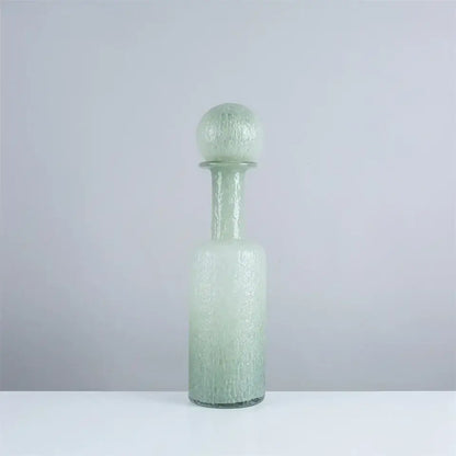 A frosted green glass decanter with a textured bubble surface and hammer lid stopper in decorbites grey round glass style