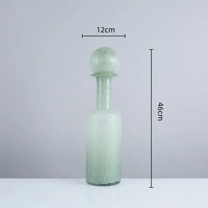 A tall frosted green glass decanter with textured surface and spherical hammer lid stopper in decorbites grey round glass set