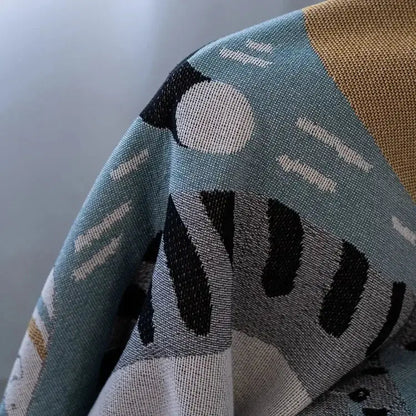 Halloween style tassel throw blanket with teal beige and black geometric pattern and textured woven fabric