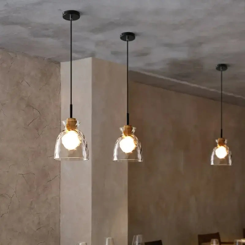 Three modern decorbites clear glass pendant lights with cork accents hang from black cords against a textured ceiling