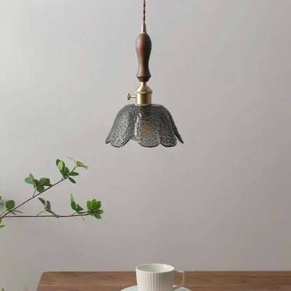 A delicate hammered gray glass led pendant lamp with textured petals, polished brass fixture, and wooden handle for living room lighting