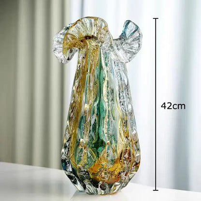 A tall hand blown glass vase with a colorful flower edge in amber and emerald hues for dining room decor