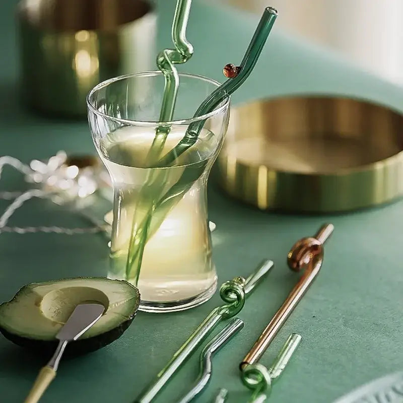 A clear glass tumbler with light beverage and two hand blown colorful twisted decorbites glass straws with red bead