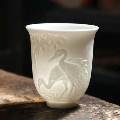 A delicate white porcelain tea cup with hand carved crane and bamboo designs in a translucent white jade tea cup set