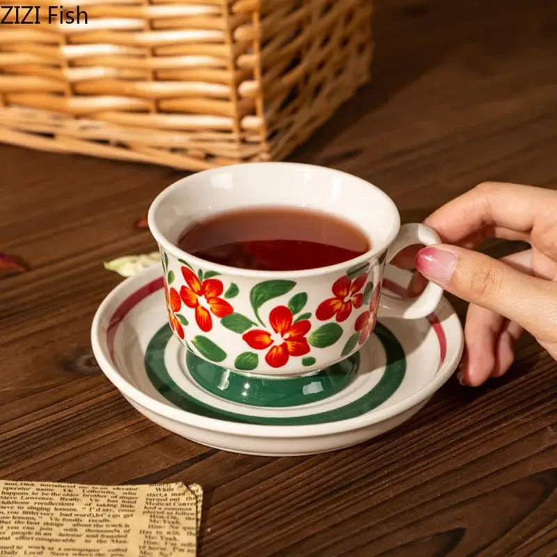 White ceramic teacup with red and green decorbites flowers pattern resting on matching flowers pattern ceramic saucer