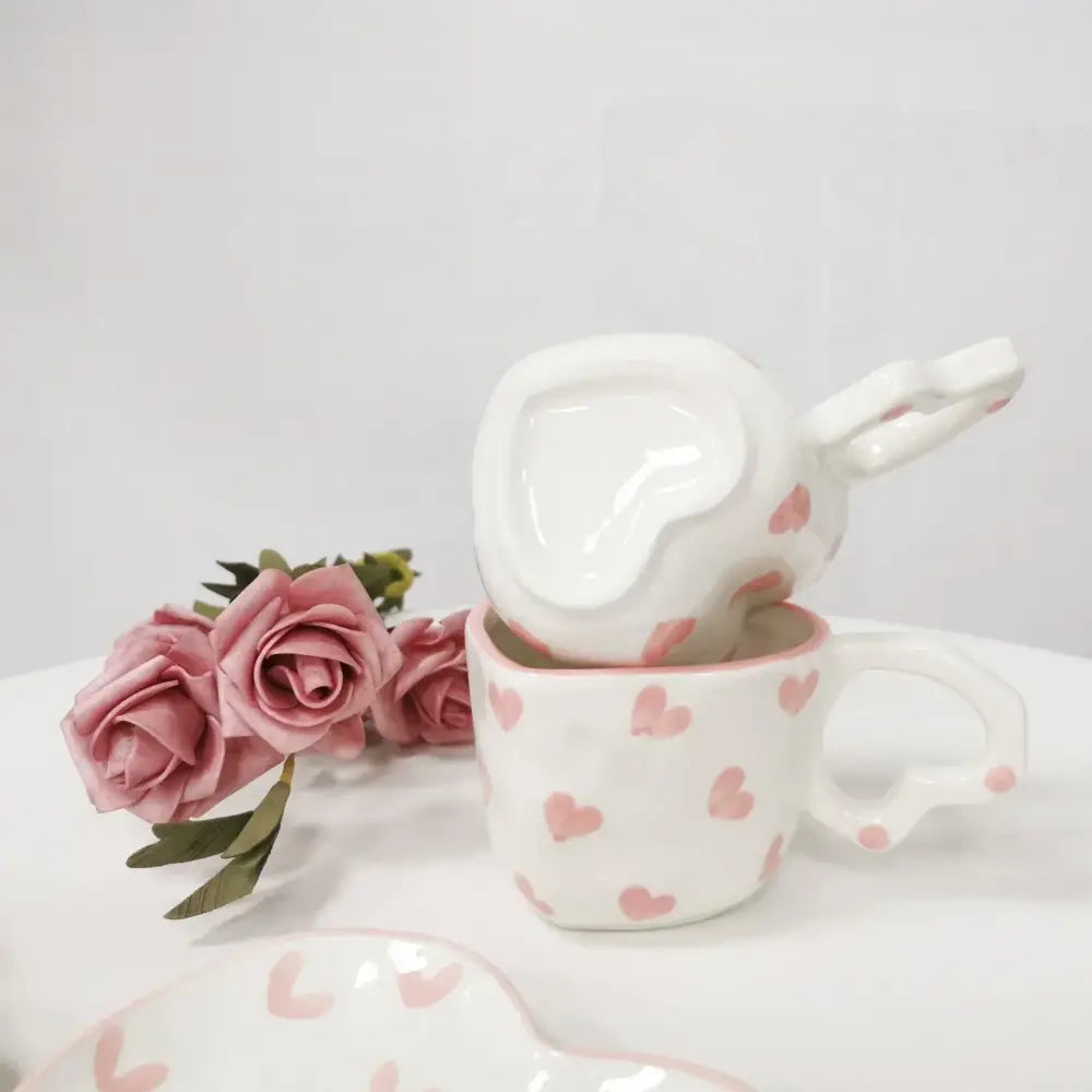White ceramic love mug set with hand painted heart handles and pink polka dot design stacked in kitchen saucer set