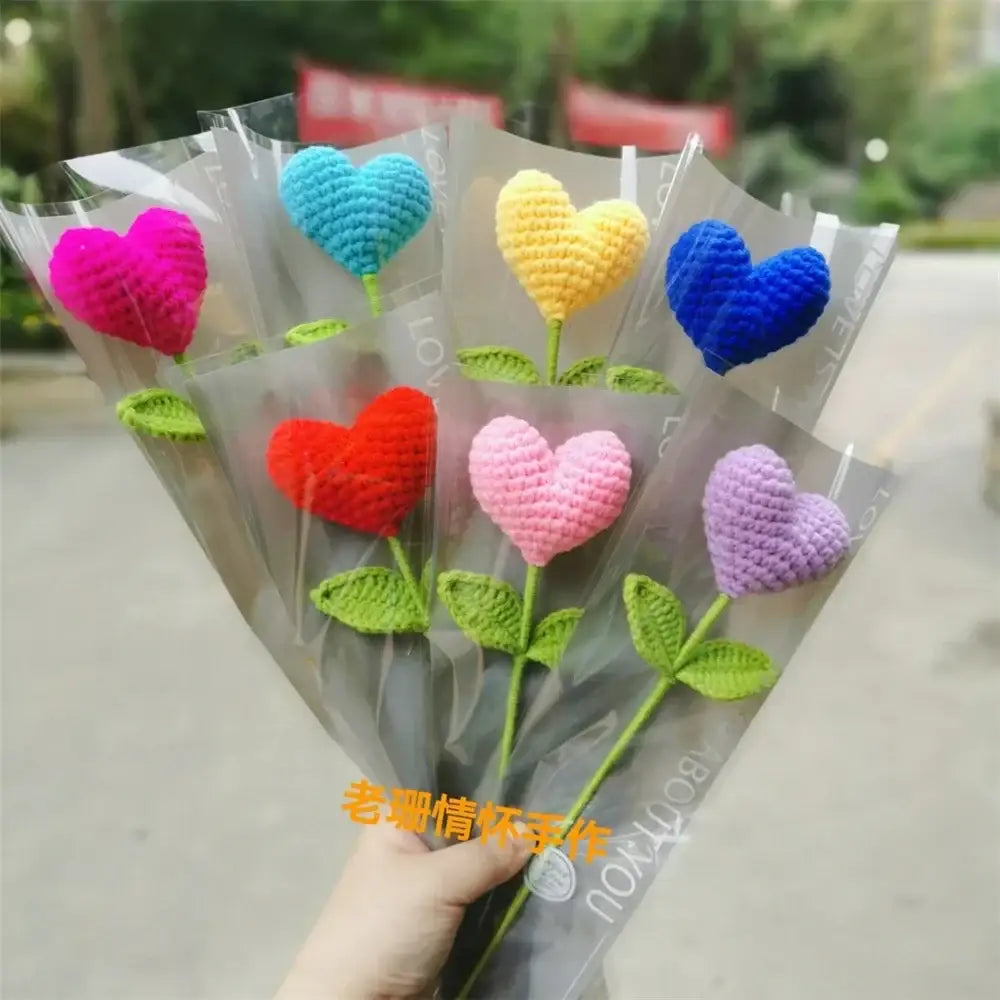 A hand woven love heart yarn crochet flower bouquet with vibrant pink blue yellow red and purple heart-shaped flowers