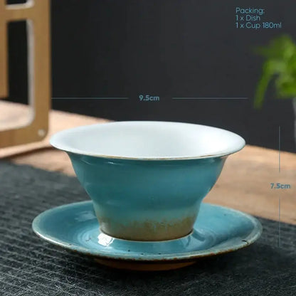 Turquoise ceramic latte coffee cup with white interior and gold rim resting on matching saucer in dining room