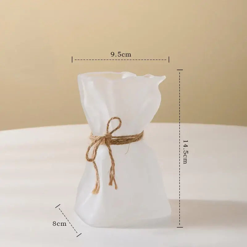 A frosted white handcrafted clear glass folded road vase shaped like a tied fabric sack with rustic twine bow decorbites clear glass