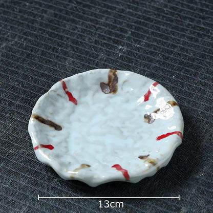 A delicate white ceramic dish with a scalloped edge and irregular red and brown glaze streaks complements hammer pattern porcelain mugs