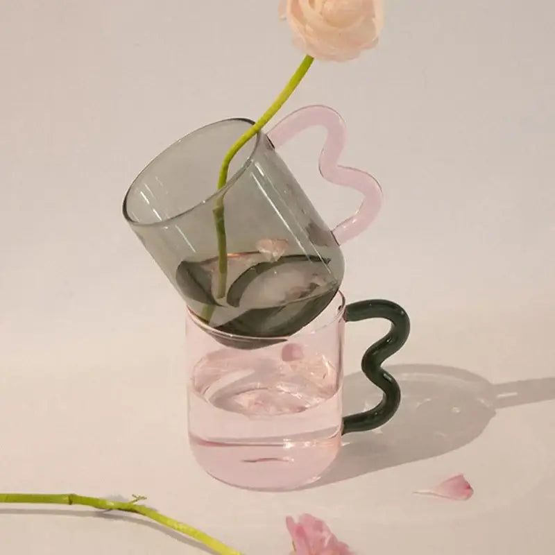 Handmade glass mug by decorbites in muted gray and soft pink with heart-shaped handle holding a single rose