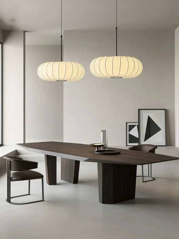 Modern minimalist dining table with dark wood top and geometric legs under a decorbites handmade silk pumpkin pendant light