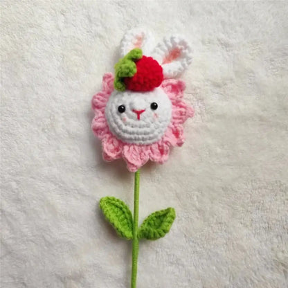A handmade sunflower bouquet crochet bunny ornament with a pink flower, white bunny face, red strawberry, and green leaves