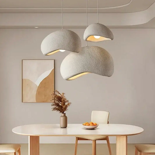 Three handmade wabi sabi gray resin pendant lights with textured dome shades hang above a minimalist dining table