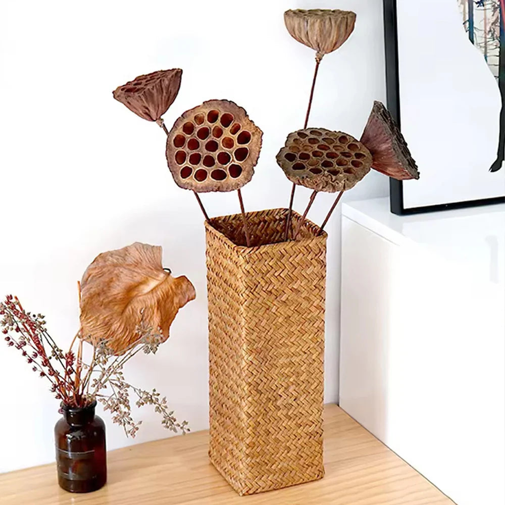 Handmade tall rectangular woven straw vase holding dried lotus seed pods for creative room flower arrangement