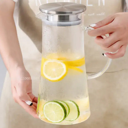 Clear glass pitcher water carafe with stainless steel lid and handle filled with lemon and lime slices in icy water