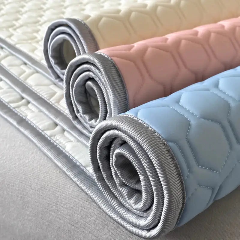 Three rolled-up hexagonal quilted bed sheet set mats in pastel cream pink and light blue with gray binding
