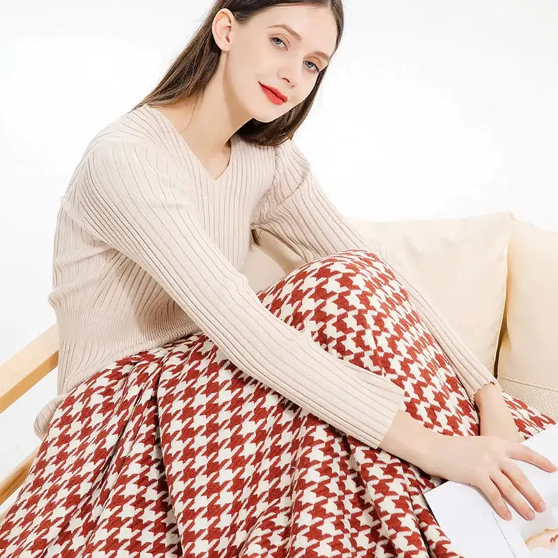 A woman wearing a cream sweater with red and white pants next to a decorbites houndstooth throw blanket with fringe