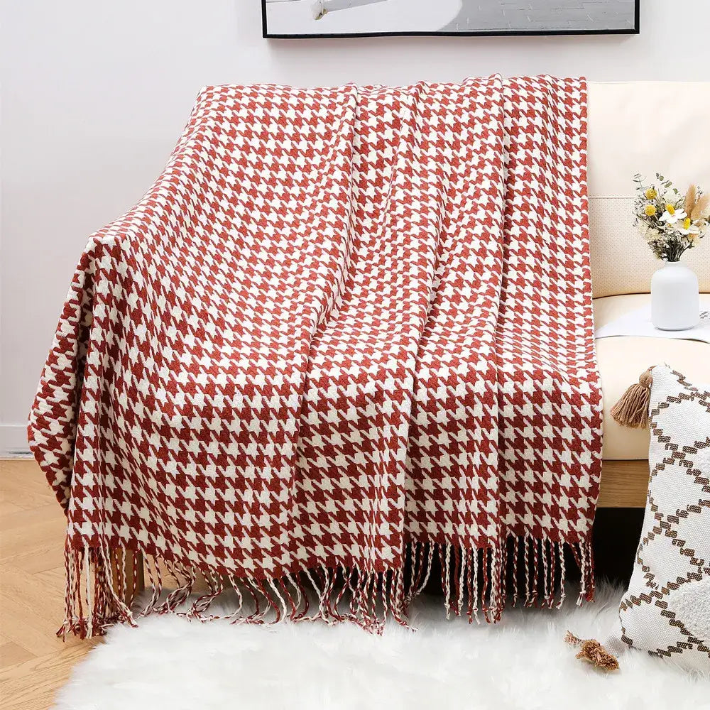 A cozy red and cream houndstooth throw blanket with fringed edges draped over a sofa for decorbites houndstooth throw decor