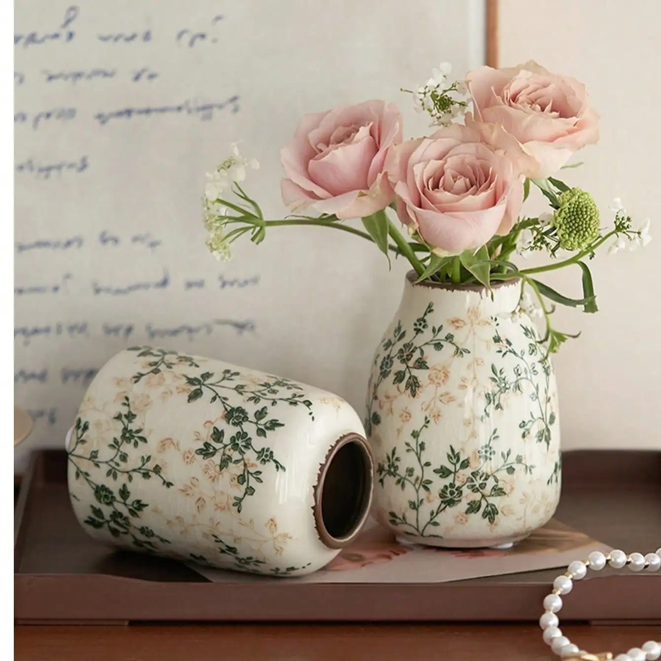 White ceramic crackle vase with green beige floral pattern standing holding pink roses and one lying on its side