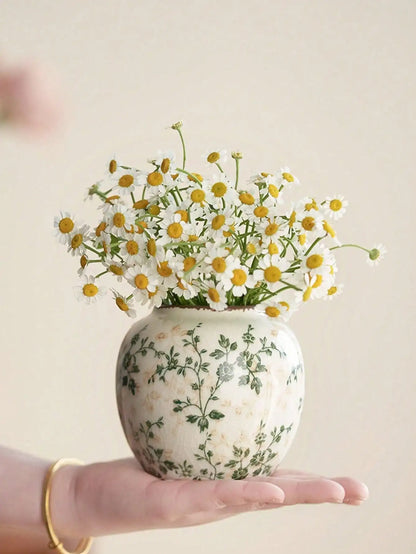 A delicate white crackle vase with green floral patterns holds fresh daisies for home or office decoration