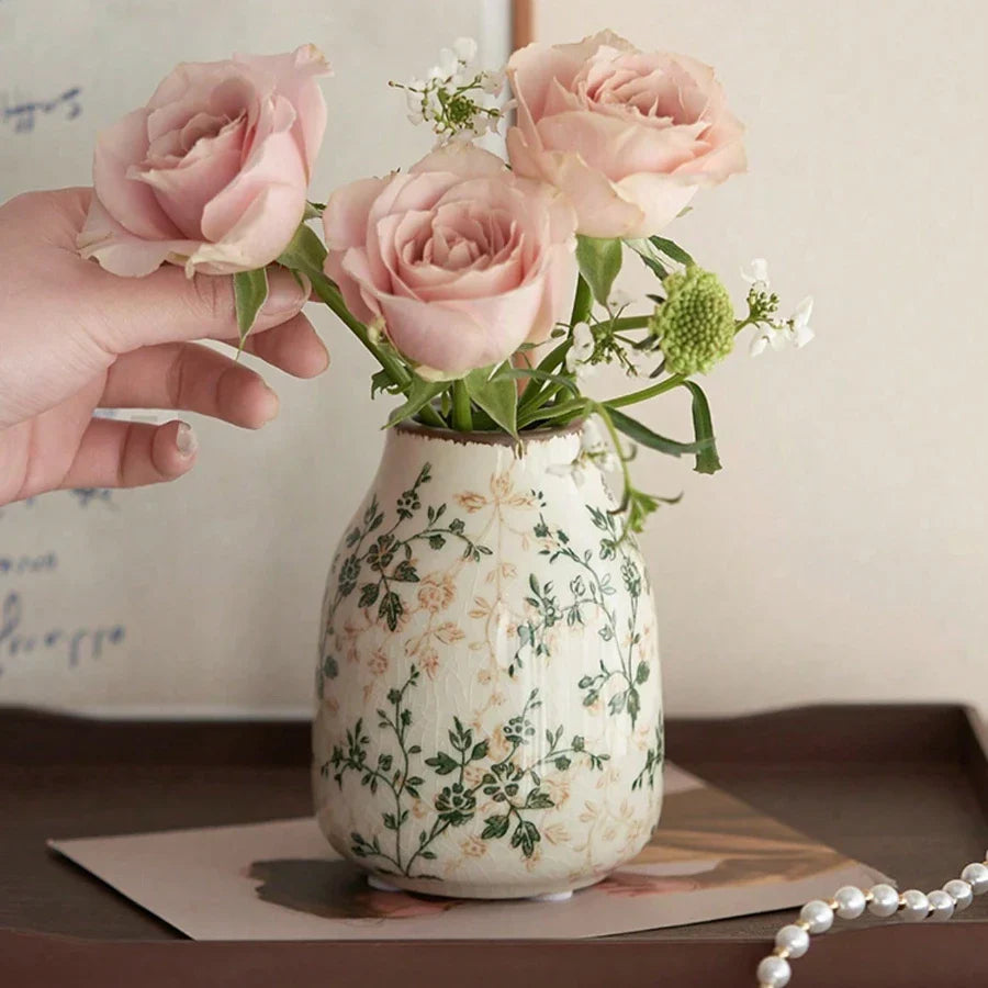 A white ice crackle ceramic vase with green beige floral patterns holding soft pink roses for home decor