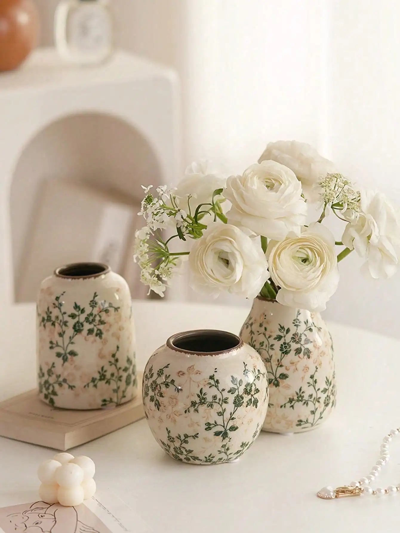 Cream-colored handmade crackle vase with green floral patterns holding white ranunculus for home decoration