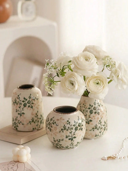 Cream-colored handmade crackle vase with green floral patterns holding white ranunculus for home decoration