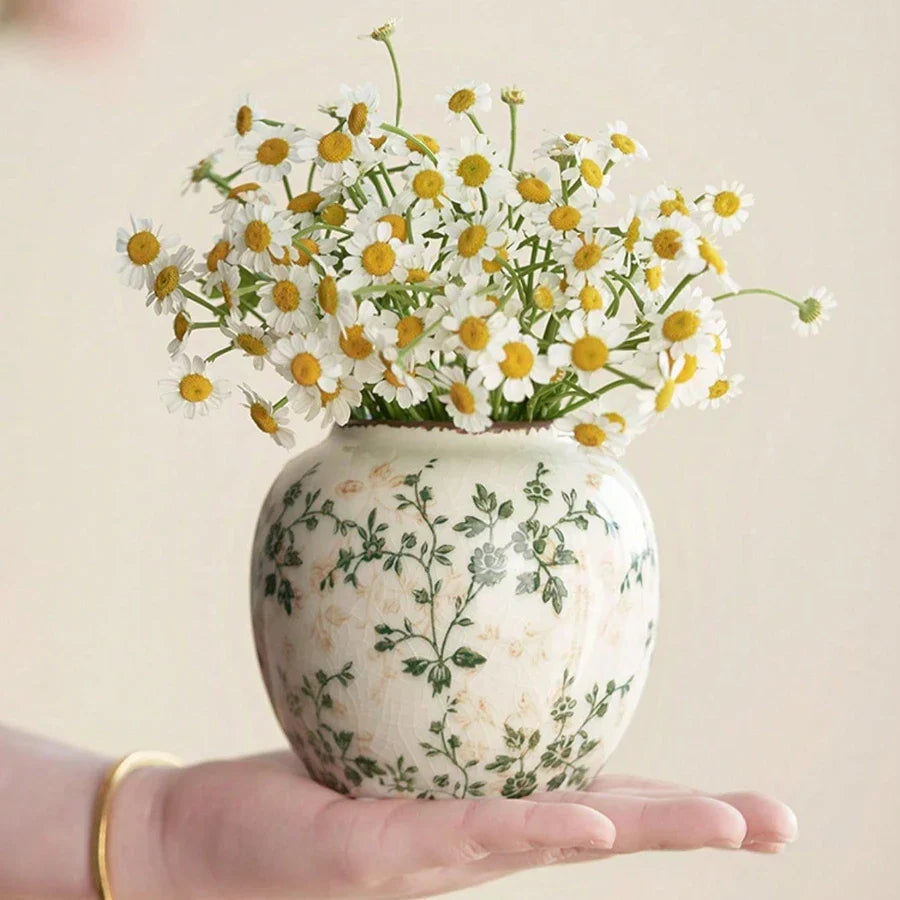 A cream-colored crackle vase with green floral patterns holding white daisies for home or office decor