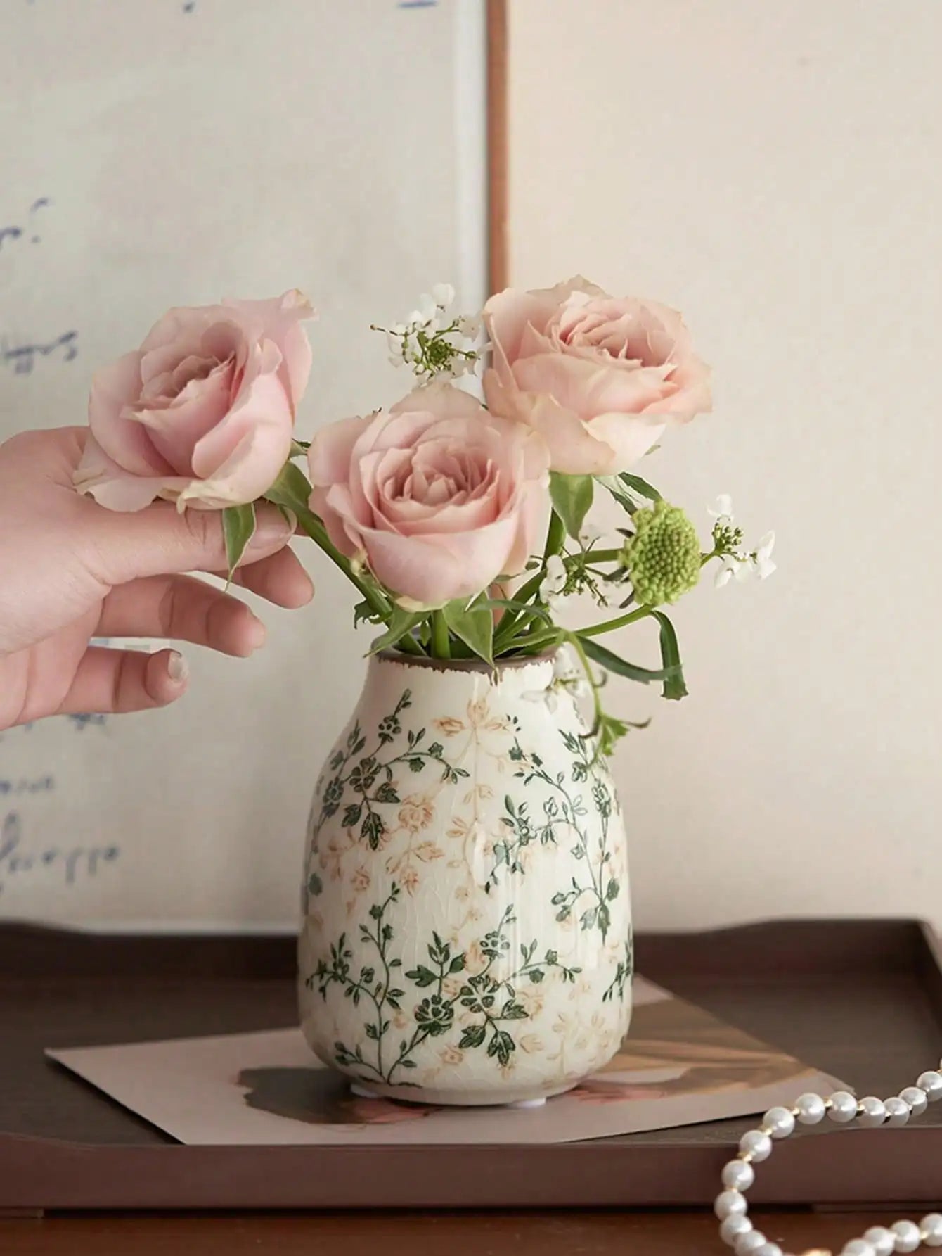 A cream-colored crackle vase with green floral pattern holding pink roses for home or office decoration