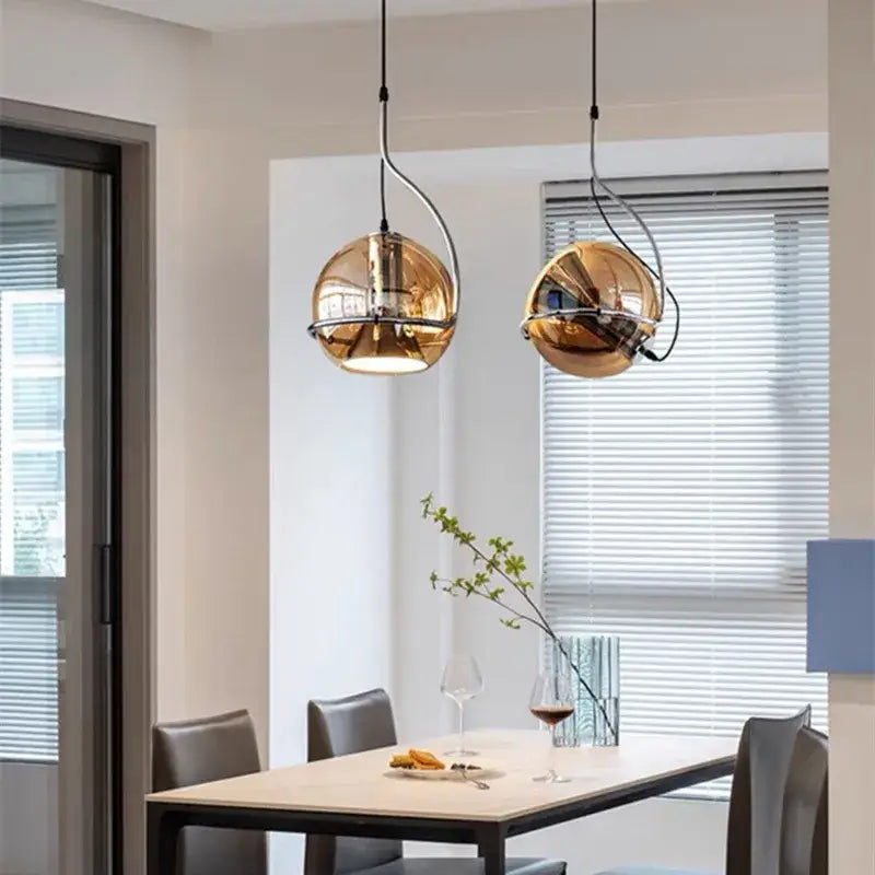 Two sleek spherical gold pendant lights with reflective finishes hang above a dining table decorbites industrial amber glass pendant light