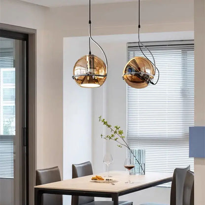 Two sleek spherical gold pendant lights with reflective finishes hang above a dining table decorbites industrial amber glass pendant light