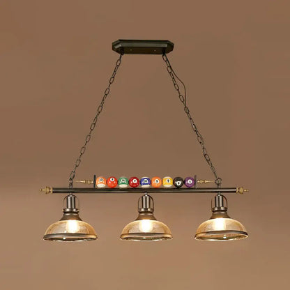 Industrial style three-light pool table lamp with black metal frame brass accents amber glass shades and billiard ball deco
