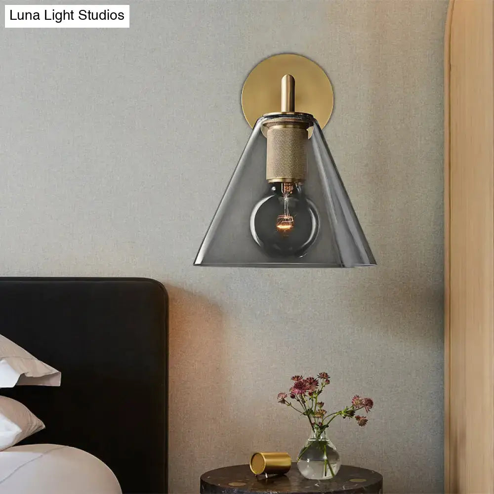 A modern industrial wall lamp with a gold-toned brass backplate and clear glass fixture type shade