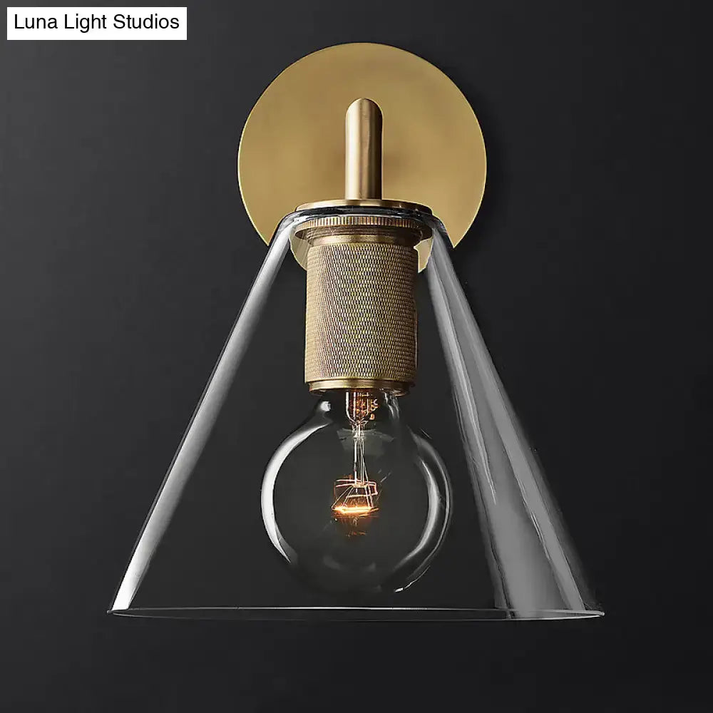 Brass-finished wall lamp with textured cylindrical base clear glass conical shade and exposed filament bulb fixture type