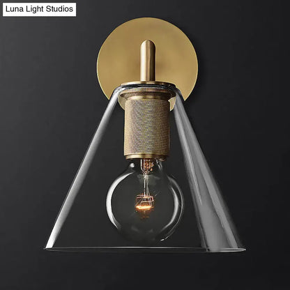 Brass-finished wall lamp with textured cylindrical base clear glass conical shade and exposed filament bulb fixture type