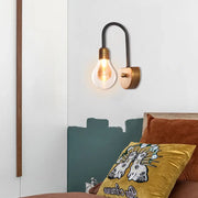 Industrial black and brass wall lamp with exposed filament bulb and curved arm suitable for bedroom light fixture