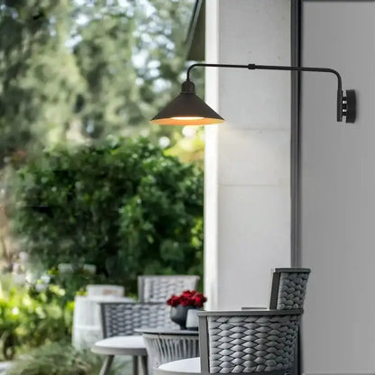 Black wrought iron wall lamp with conical shade and telescopic swing arm emitting warm light for living room