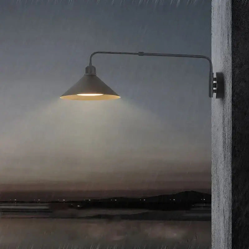 A sleek black matte telescopic swing arm wall lamp with conical shade emits warm light against twilight backdrop