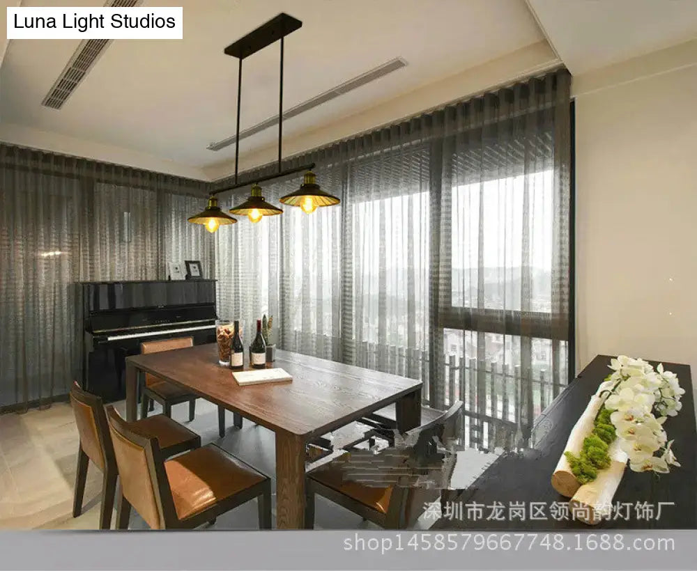 Industrial black metal island pendant with three brass cone shade fixtures hanging above wooden dining table