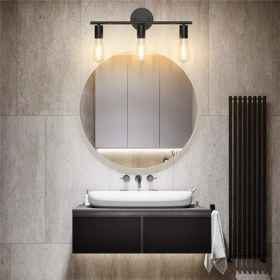 Black metal wall lamp with three exposed filament bulbs mounted above a round mirror for bathroom use
