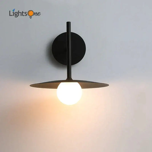 Black minimalist wall lamp with circular base and disc shade featuring a glowing bulb in decorbites industrial style wall design