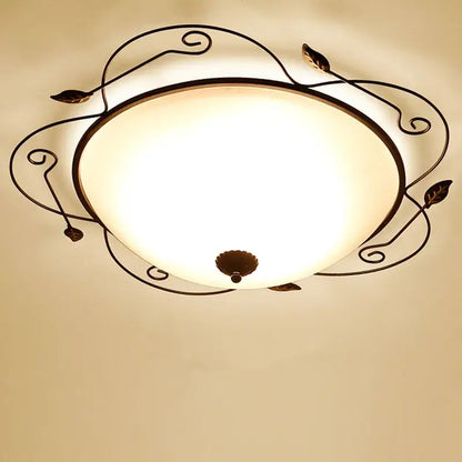 A warm-toned glass round ceiling light with an industrial black wrought iron frame featuring leaf and scroll designs