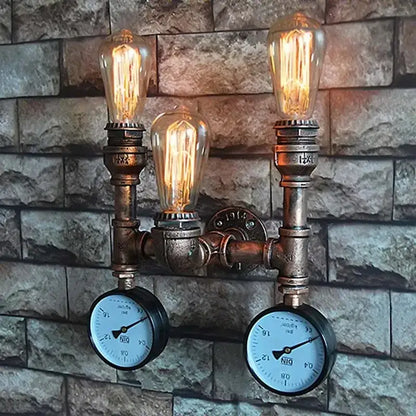 Industrial dark brass pipe wall lights with three glowing filament bulbs and two pressure gauges on brick background