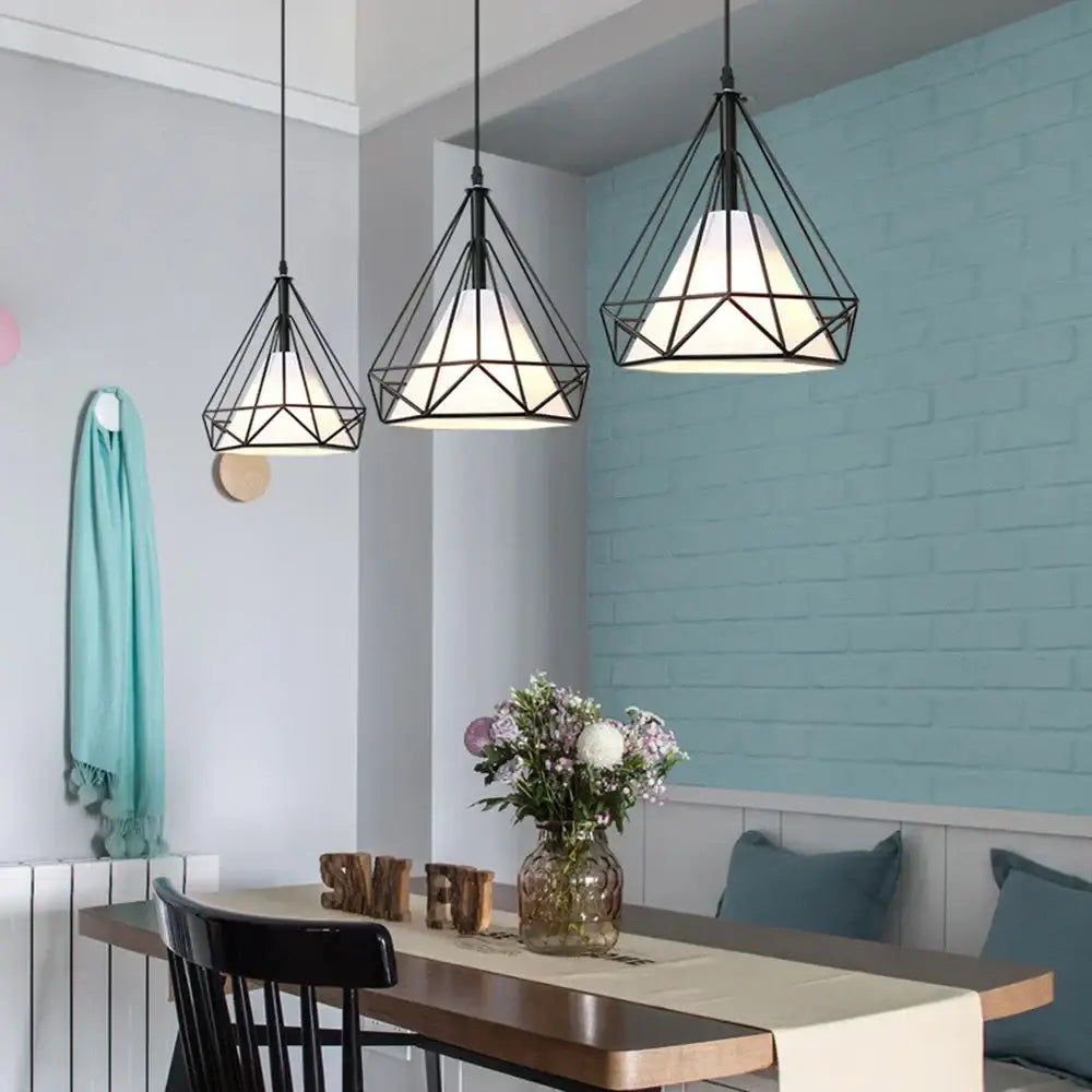 Three black geometric diamond cage pendant lights with white glass shades hang above a dining table for kitchen and living room