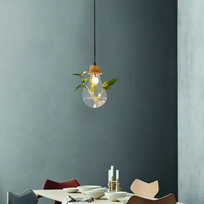 Industrial glass and wood pendant light kit with exposed bulb and green plant stems for dining room illumination