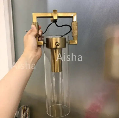 A modern industrial glass wall lamp with brass frame, clear glass cylinder, and textured gold knobs for bedroom decorbites industrial glass